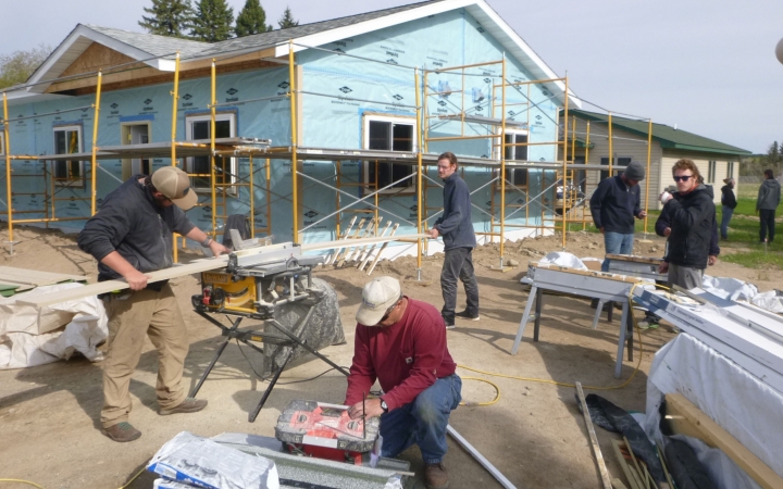 A group of people use tools while building a house during a service project with outward bound.